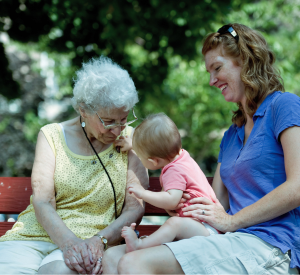 Grandmother sitting on a bench with daughter, playing with her granddaughter