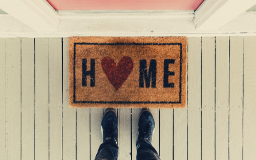 Person standing by a doormat that says Home on it
